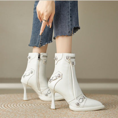 White high-heeled ankle boots with decorative elements worn by a person on a neutral background.