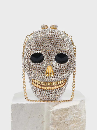 A rhinestone-encrusted skull head clutch bag with a detachable gold chain.
