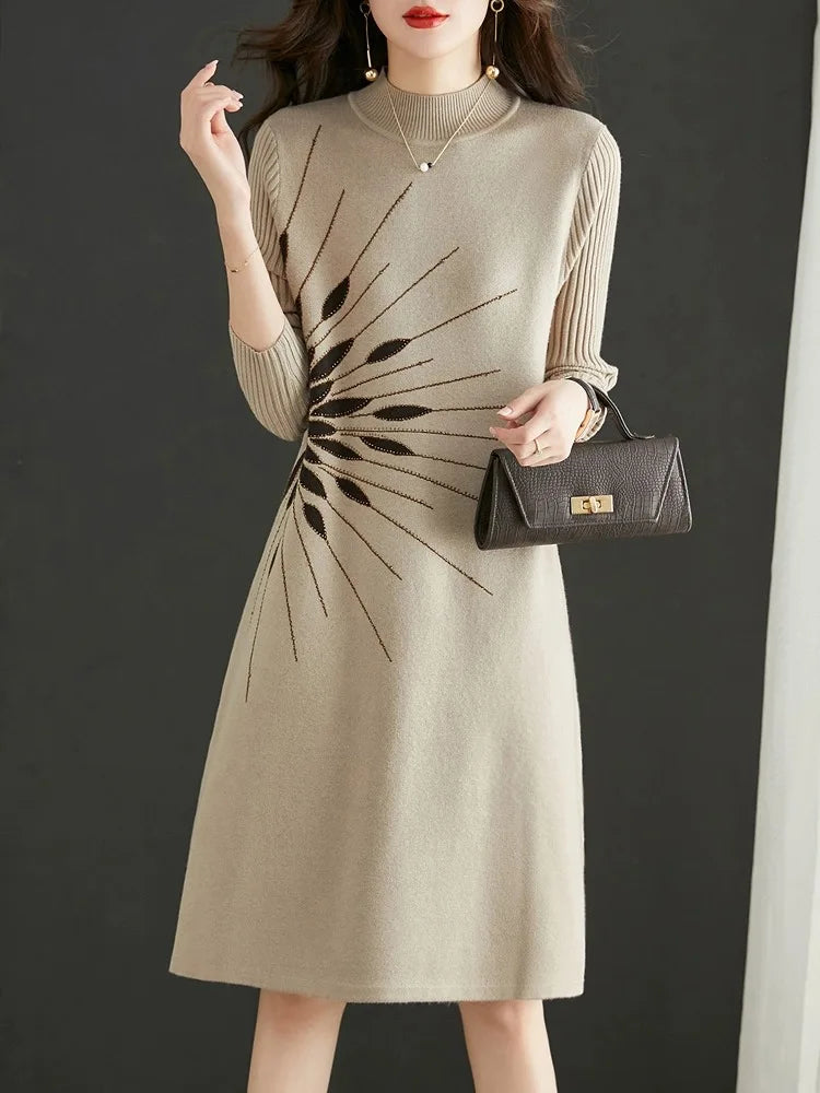 Woman wearing a beige dress with a black abstract pattern, holding a black handbag against a dark background.