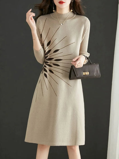 Woman wearing a beige dress with a black abstract pattern, holding a black handbag against a dark background.